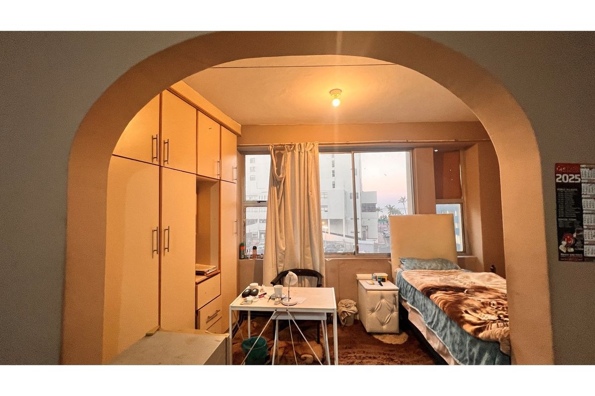 A bedroom featuring built-in wooden wardrobes, large windows providing natural light, and an arched entryway.