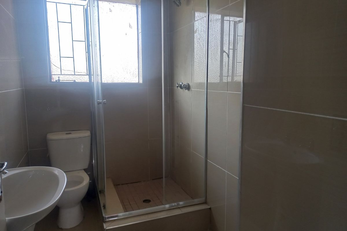 A functional bathroom featuring a glass-enclosed shower, a pedestal basin, and a standard toilet with neutral wall tiling.