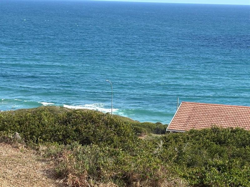 A scenic view of the ocean from the vacant residential property, featuring coastal vegetation and a partial view of a neighboring roof.