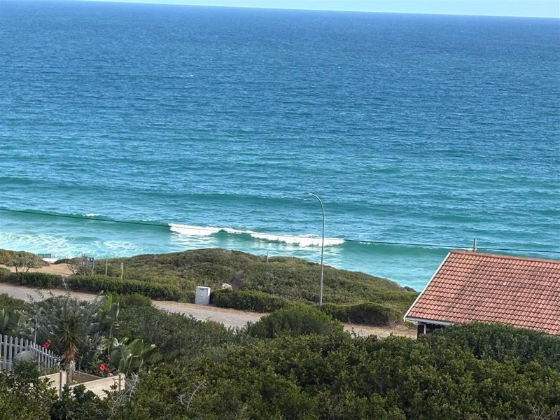 A scenic elevated view overlooking the coastline, featuring natural vegetation, a nearby road, and a clear perspective of the ocean.