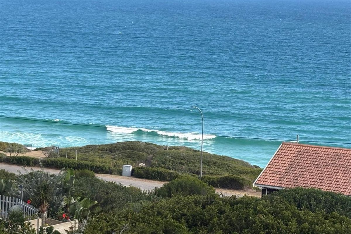 A scenic elevated view overlooking the coastline, featuring natural vegetation, a nearby road, and a clear perspective of the ocean.