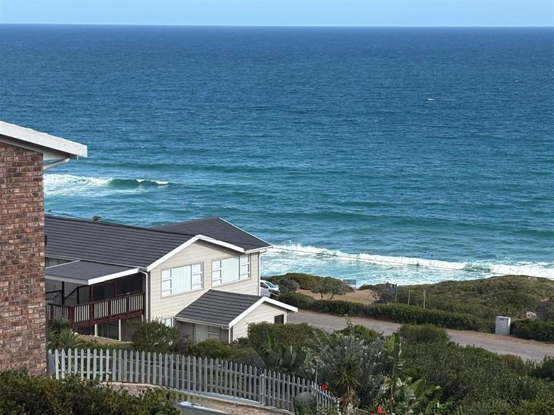 Elevated view overlooking the coastline and ocean, featuring a residential property with a tiled roof and balcony.