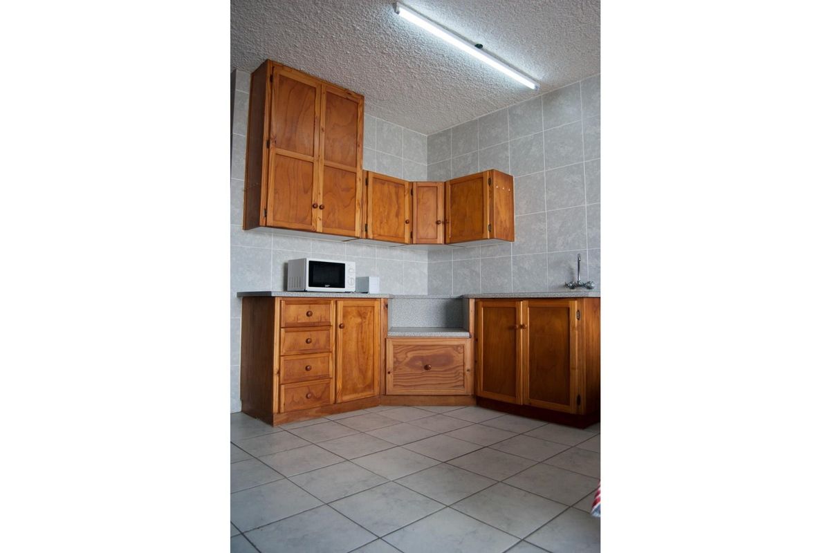 A functional kitchen area featuring traditional wooden cabinetry, tiled splashbacks, and tiled flooring, providing a classic and practical workspace.