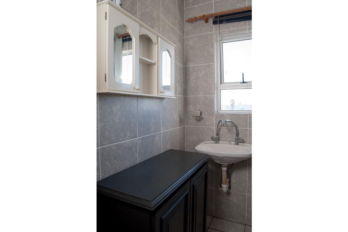 A compact bathroom or utility space featuring grey wall tiling, a wall-mounted basin, and built-in cabinetry with overhead storage.