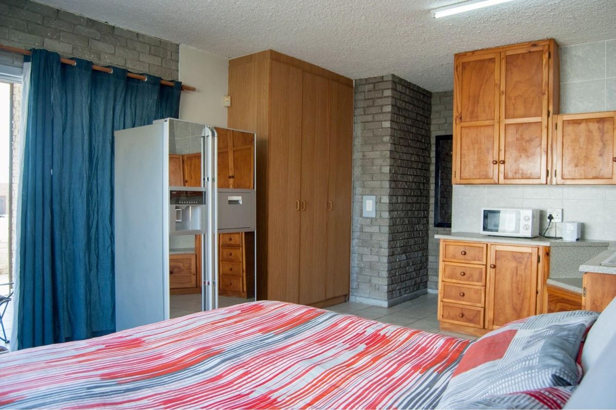 A bedroom featuring built-in wooden cabinetry, exposed brickwork, and integrated storage, offering a functional layout with direct access to an outdoor area.