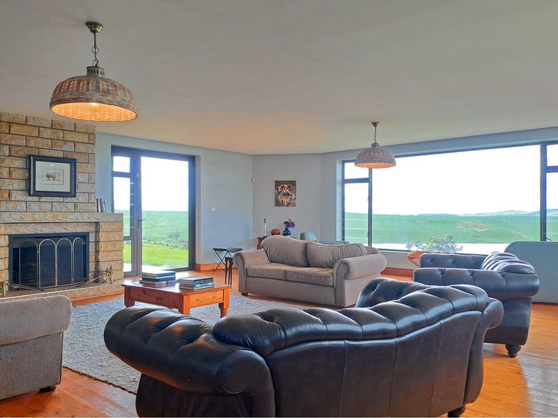 Spacious living room featuring a stone fireplace, timber flooring, and large windows offering expansive rural views and abundant natural light.