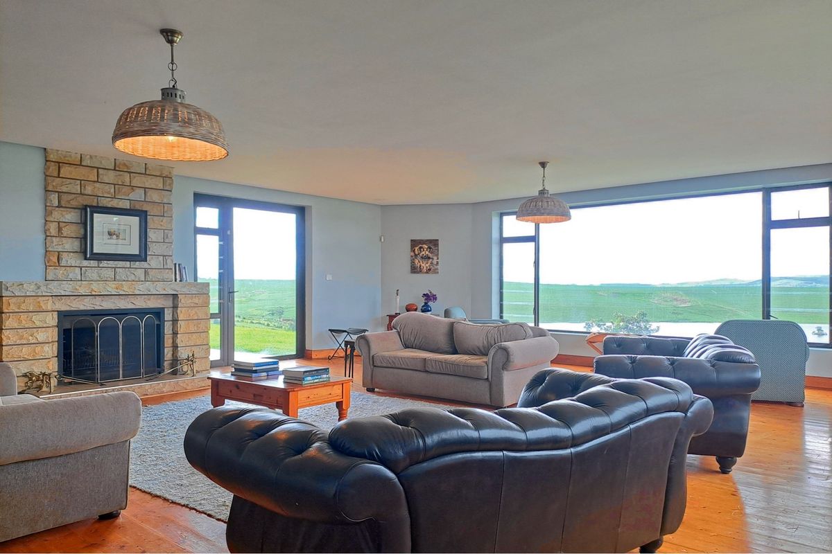 Spacious living room featuring a stone fireplace, timber flooring, and large windows offering expansive rural views and abundant natural light.