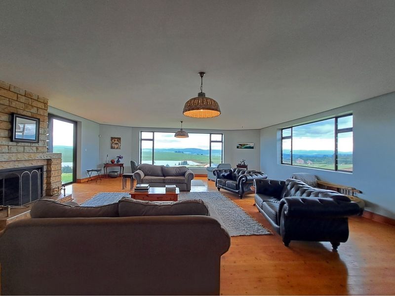 Spacious living room featuring a stone fireplace, timber flooring, and expansive windows offering panoramic countryside views.
