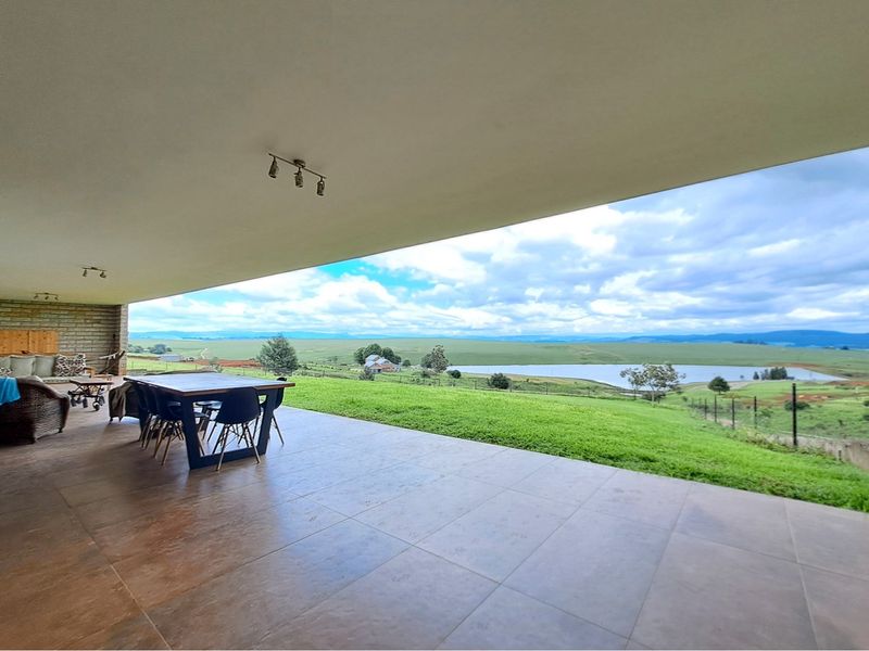 Spacious covered patio featuring tiled flooring and exposed brickwork, offering expansive views over the surrounding landscape and lake.