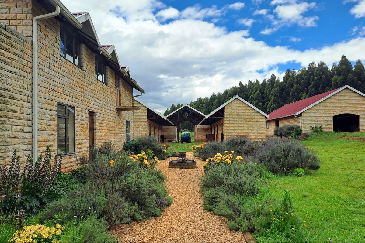A well-maintained courtyard area featuring stone-clad buildings, a central gravel pathway, a water feature, and established garden beds.