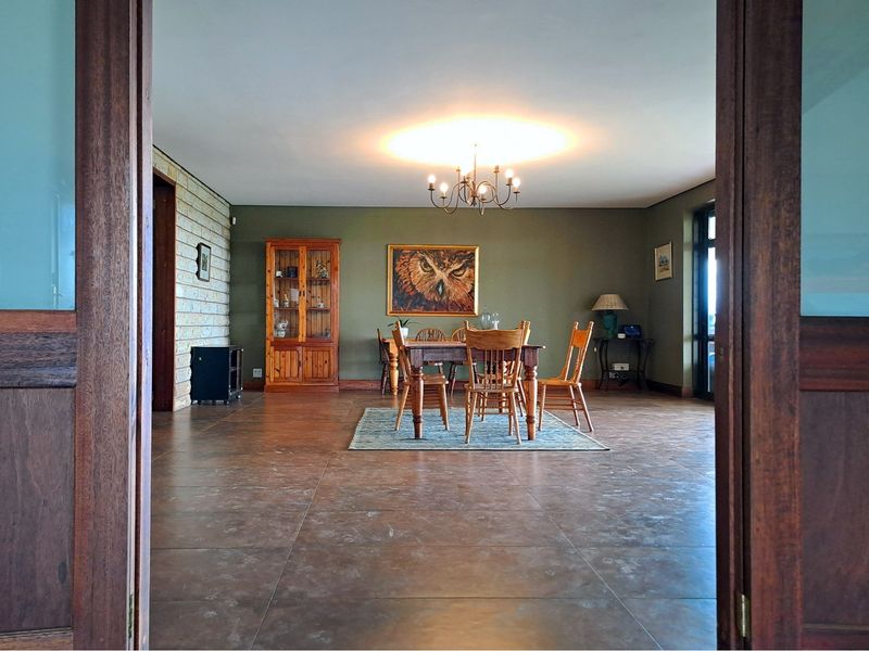 Spacious dining room featuring large format floor tiles, a stone feature wall, and a classic chandelier, viewed through double wooden doors.