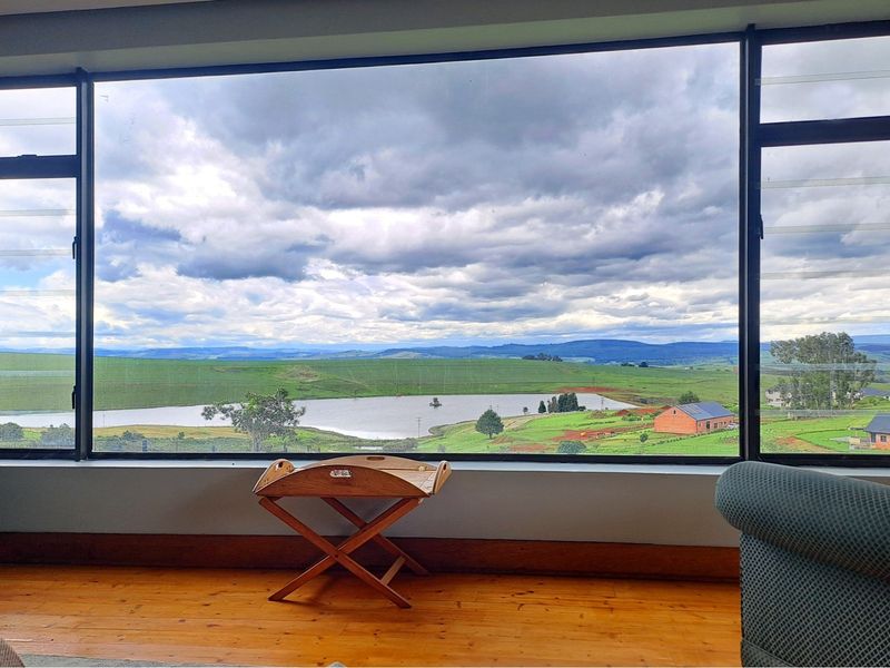 A bright living space featuring a large picture window that frames expansive views of the surrounding landscape, lake, and rolling hills.