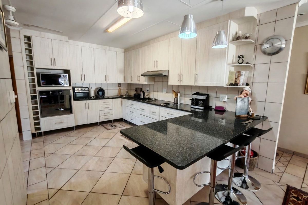 Spacious kitchen featuring light wood-grain cabinetry, dark granite countertops, a breakfast bar, and integrated oven and microwave units.