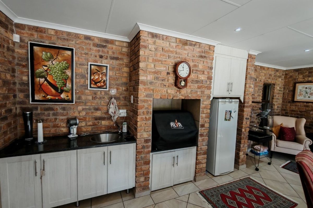 Indoor entertainment area featuring a built-in brick braai, granite countertop, stainless steel prep sink, and modern cabinetry.