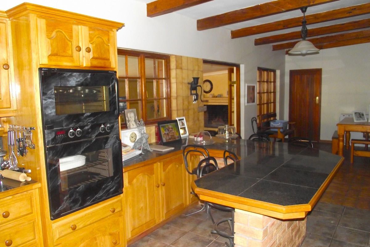 A rustic kitchen featuring wooden cabinetry, dark tiled countertops, a built-in oven, and exposed timber ceiling beams.