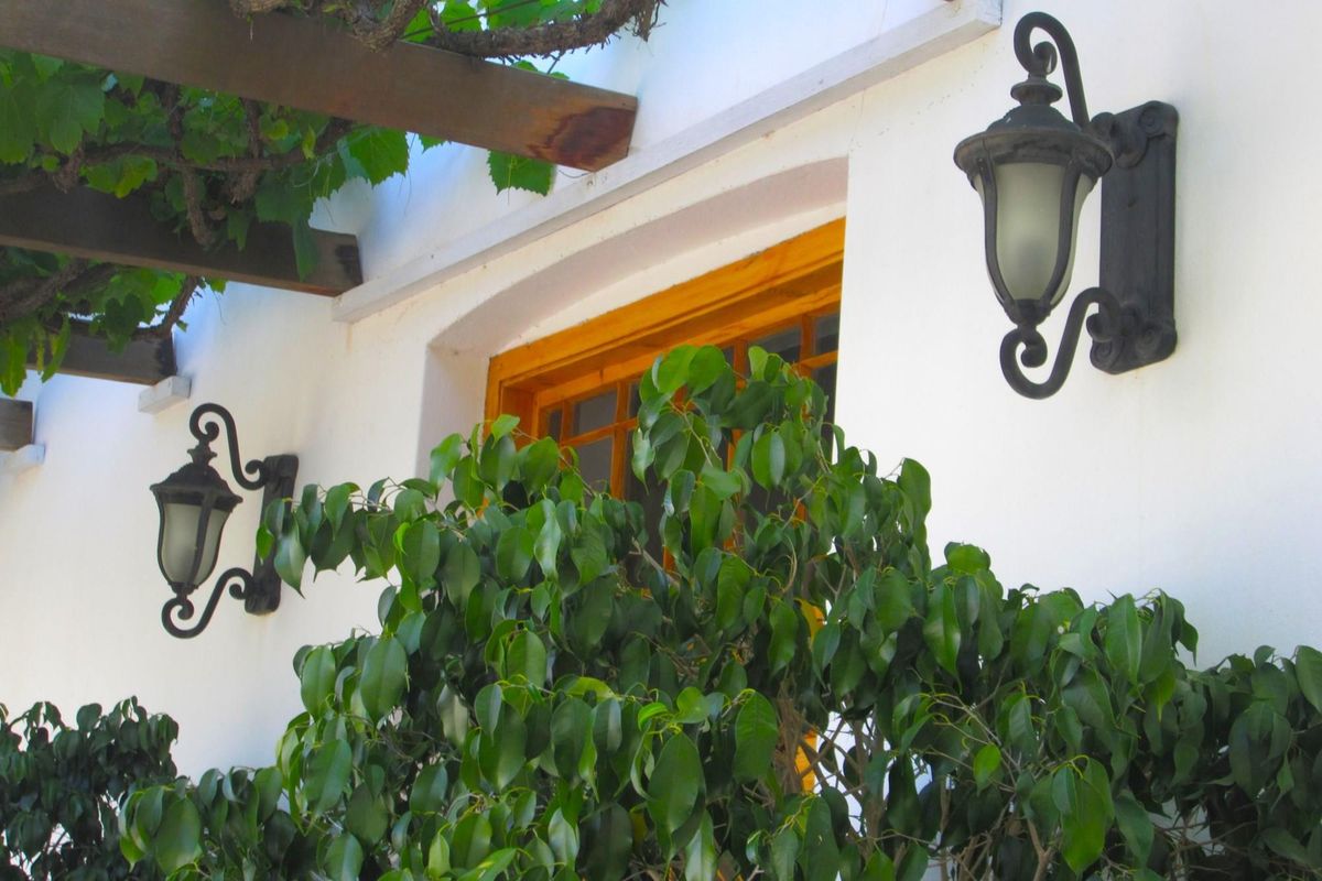 A close-up view of a white exterior wall featuring traditional wall-mounted lanterns, a timber pergola structure, and a wooden window frame.