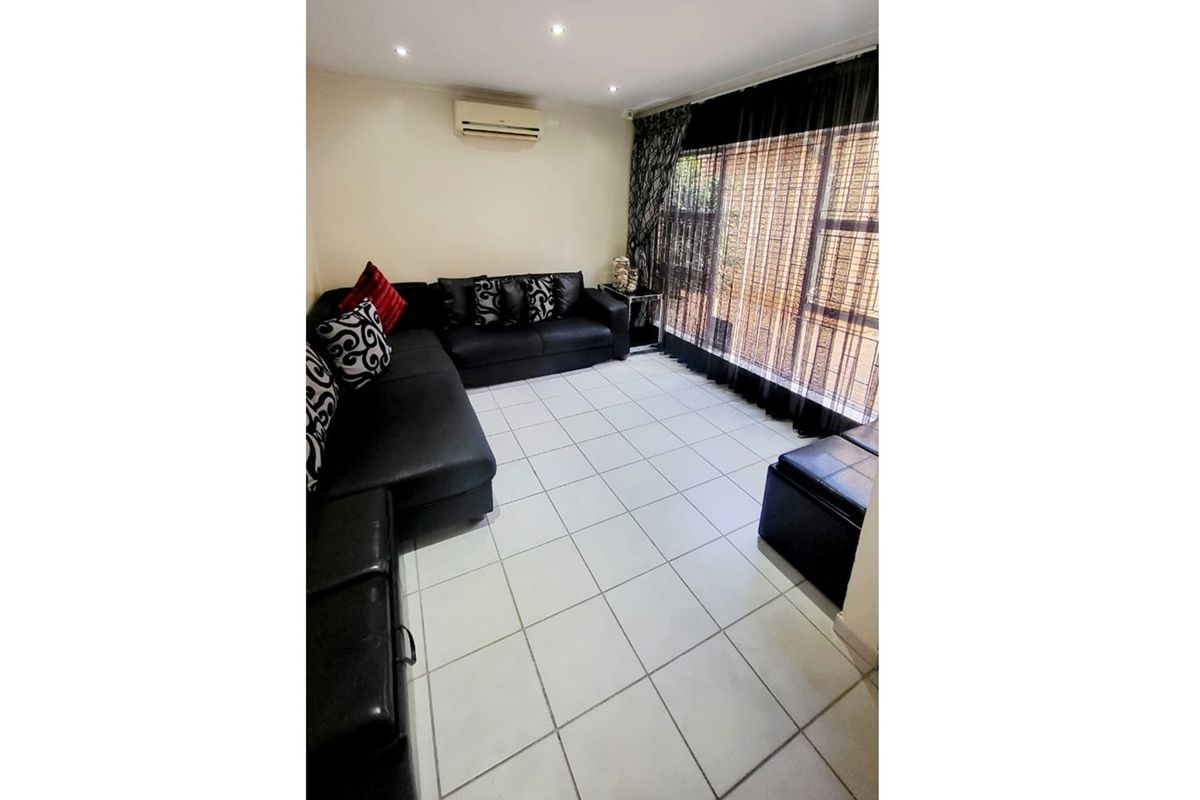 A living room featuring tiled flooring, recessed downlighting, and a wall-mounted air conditioning unit, with a large window providing natural light.