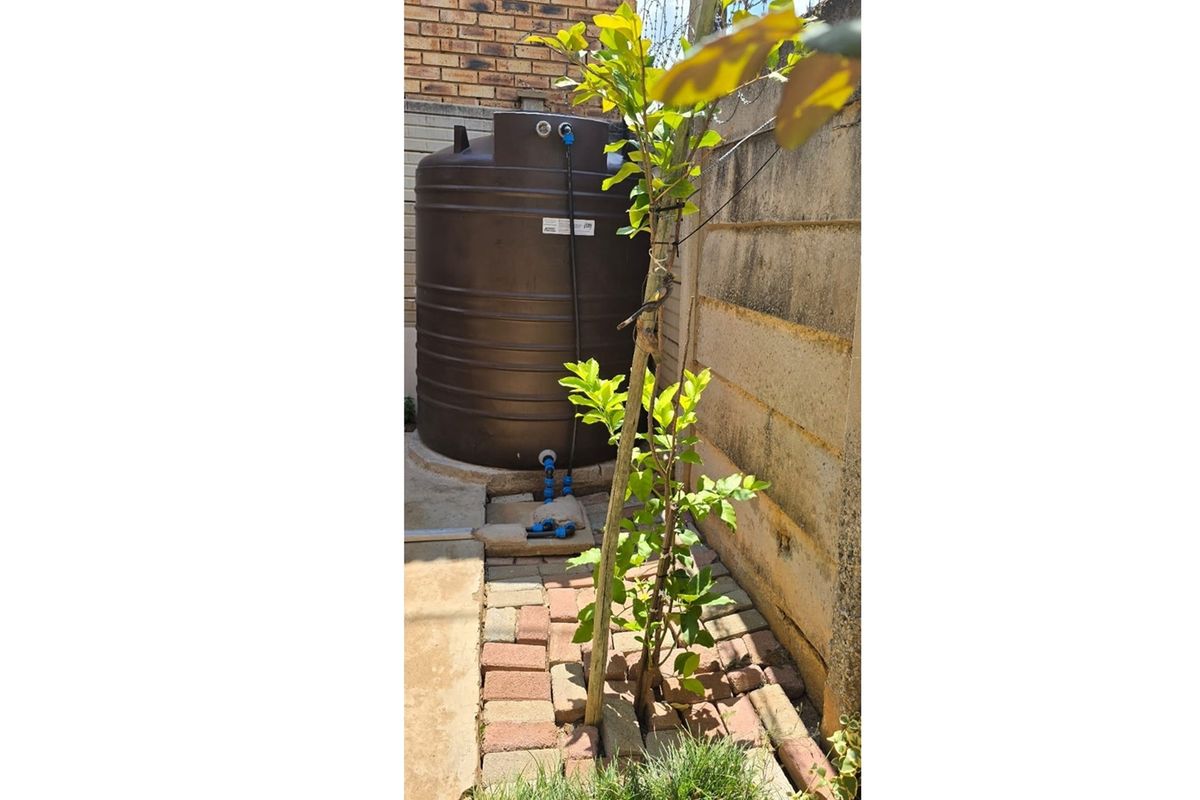 A rear exterior area featuring a water storage tank positioned against a brick boundary wall with paved ground surfacing.
