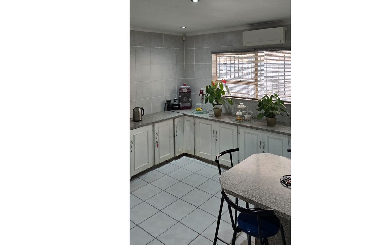 A functional kitchen featuring tiled flooring, ample built-in cabinetry, laminate countertops, and a wall-mounted air conditioning unit.
