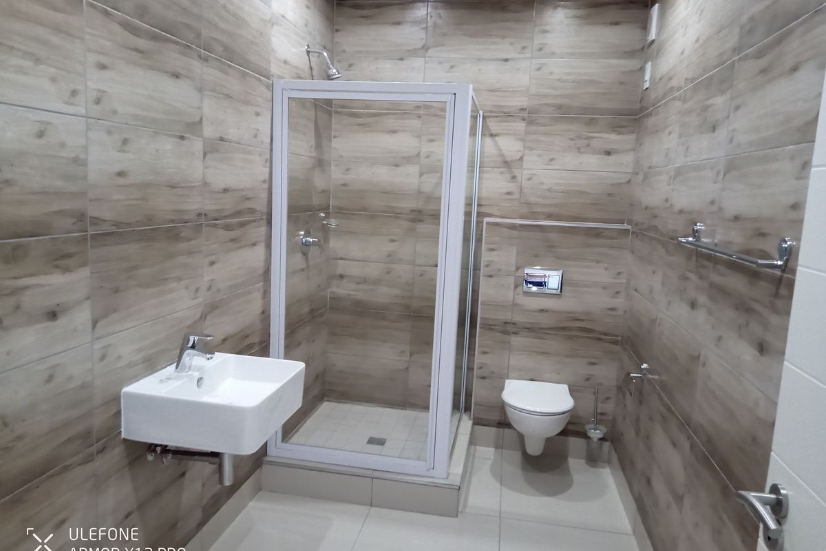 Modern bathroom featuring wood-look wall tiling, a wall-mounted basin, a glass-enclosed shower, and a wall-hung toilet.