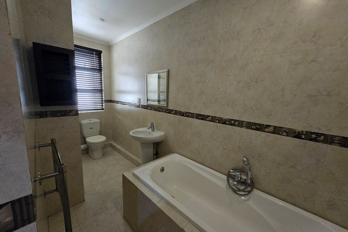 A functional bathroom featuring a built-in bathtub, pedestal sink, toilet, and tiled walls with a decorative border.