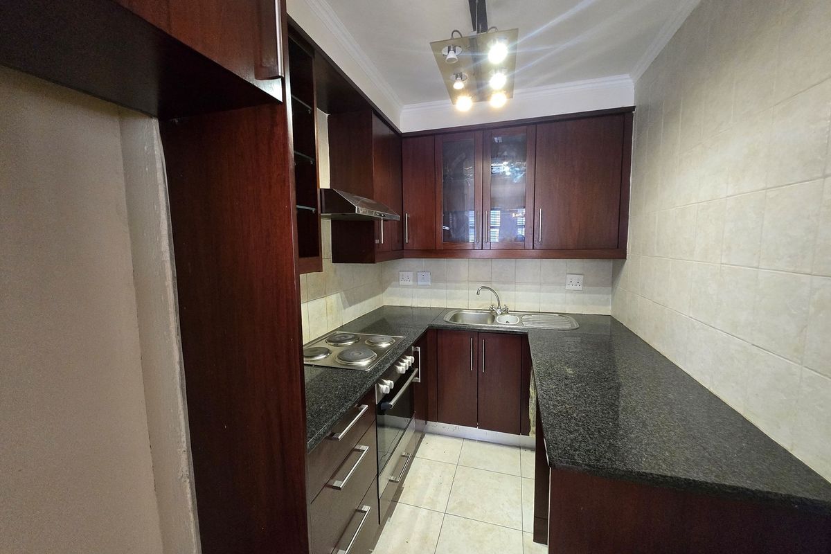 Compact kitchen featuring dark wood cabinetry, granite countertops, a built-in oven, electric hob, and stainless steel sink.