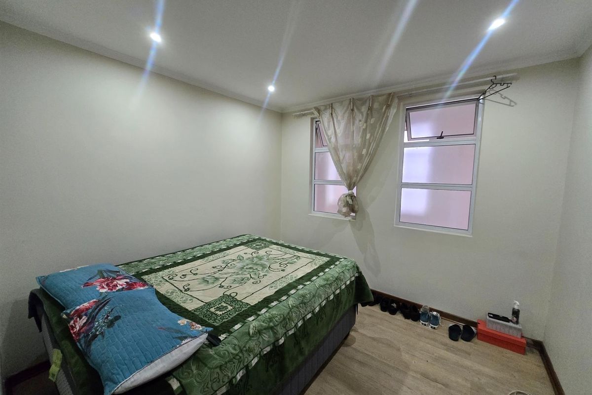 A functional bedroom featuring light-toned laminate flooring, recessed ceiling downlights, and dual windows providing natural light.