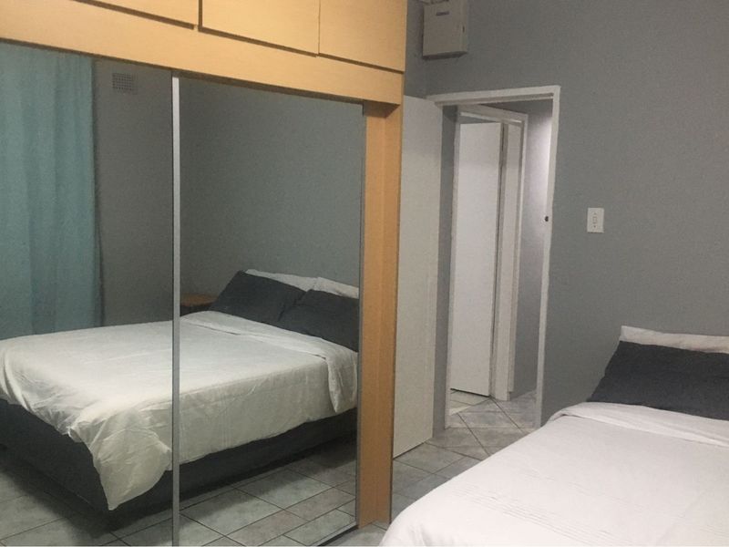 A bedroom featuring tiled flooring and a large built-in mirrored wardrobe, providing ample storage space and a functional layout.