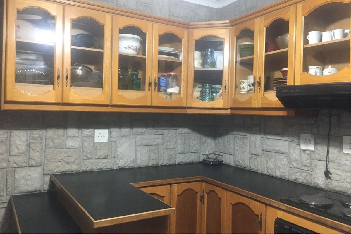 A functional kitchen featuring traditional wooden cabinetry, stone-cladding backsplash, and a dark laminate countertop with an integrated electric hob.