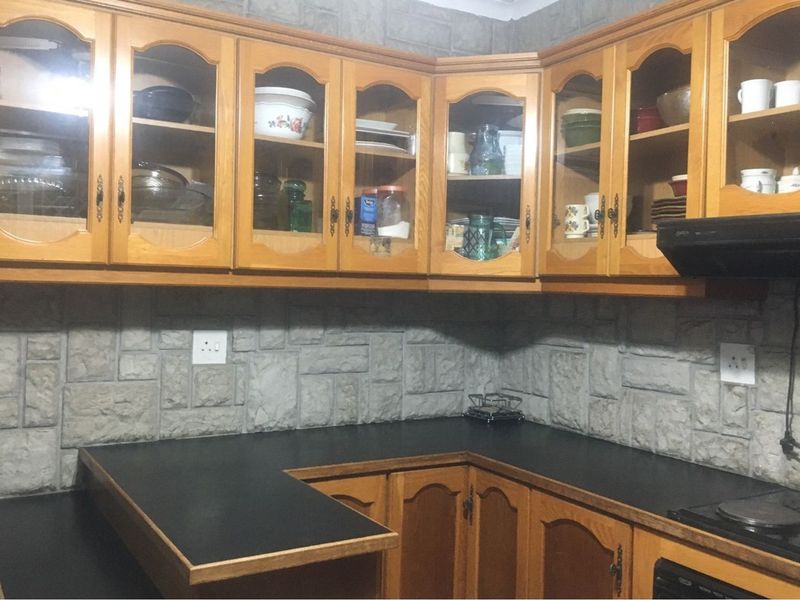 A functional kitchen featuring traditional wooden cabinetry, stone-cladding backsplash, and a dark laminate countertop with an integrated electric hob.