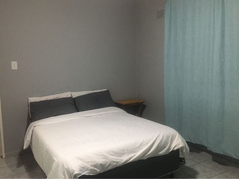 A simple bedroom featuring tiled flooring and neutral wall finishes, providing a functional space for rest.
