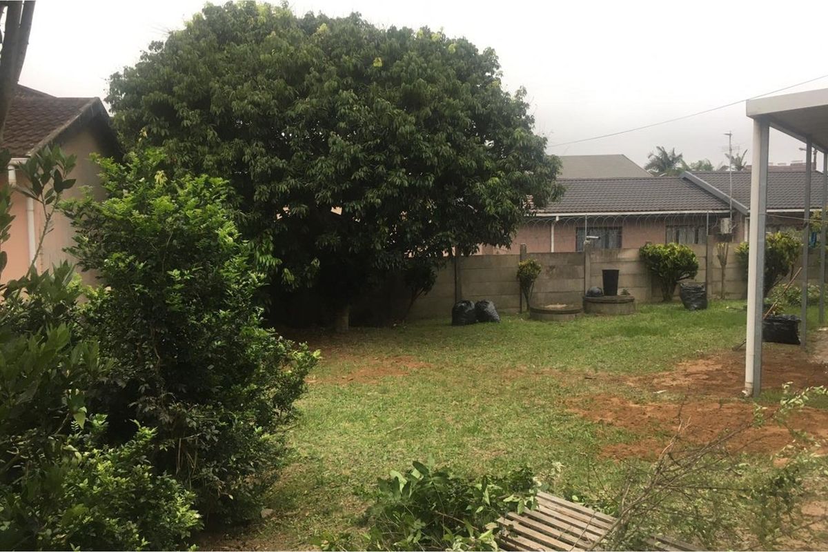 A rear garden area featuring a lawn, mature trees, and a precast concrete boundary wall with security razor wire.