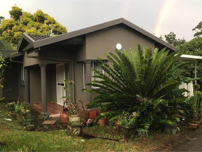 Front elevation of a single-story house featuring a covered porch with decorative columns, tiled roof, and established garden surroundings.