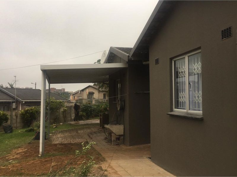 Rear exterior view of the house featuring a covered patio area, paved walkway, and a fixed concrete wash basin.