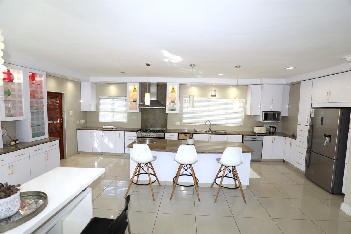 Spacious modern kitchen featuring white cabinetry, granite countertops, a central island with breakfast bar seating, and integrated stainless steel appliances.