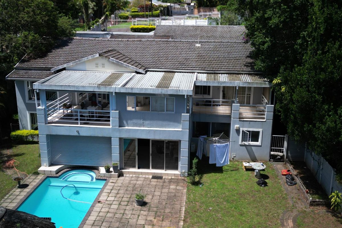 Aerial view of the rear elevation featuring a swimming pool, paved patio area, upper-level balconies, and a spacious garden.