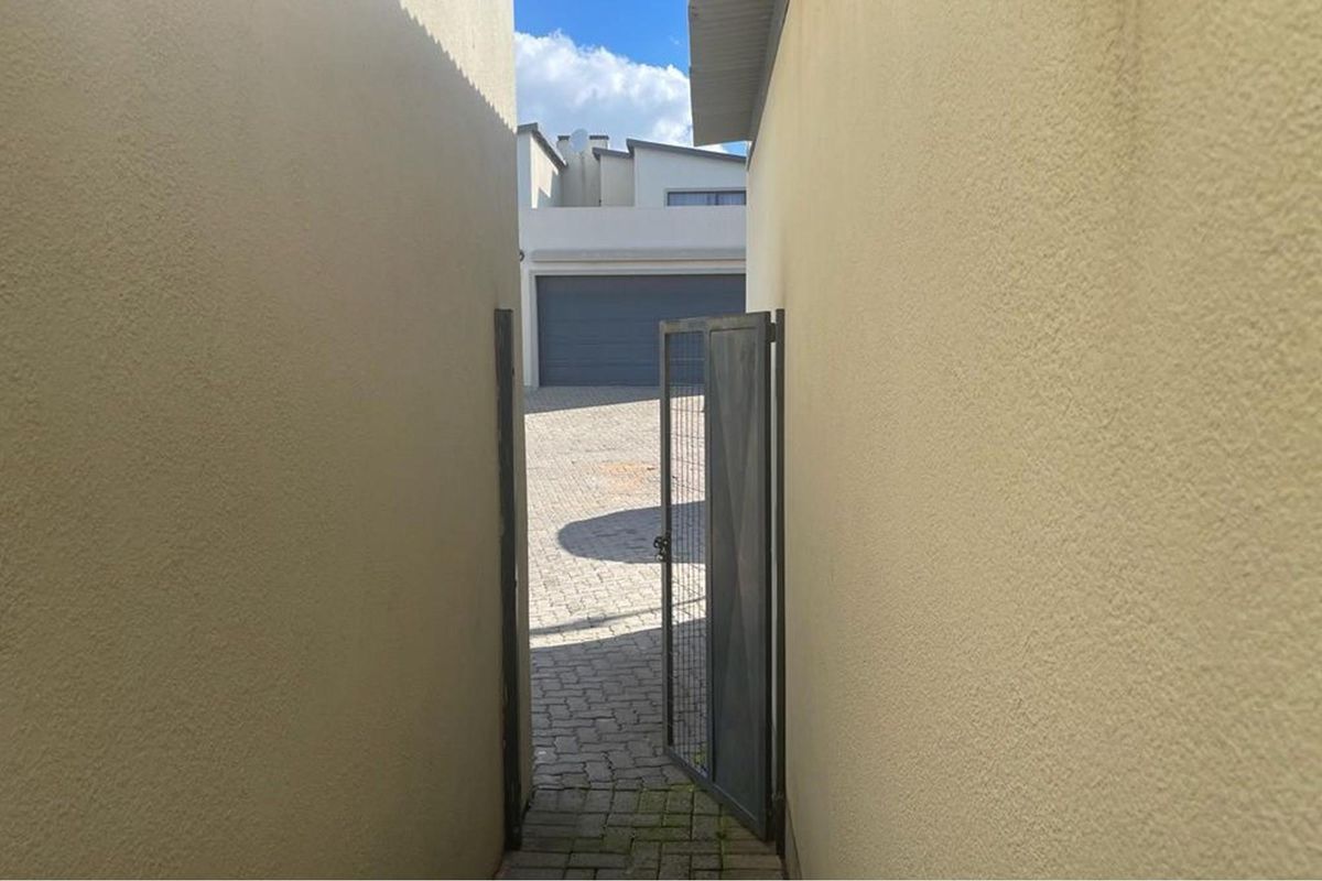 A narrow side passage with paved flooring leading to a paved courtyard area with a garage door visible in the background.