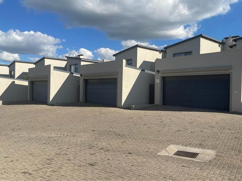Exterior view of a row of modern apartment units featuring paved driveway access and individual garage doors.