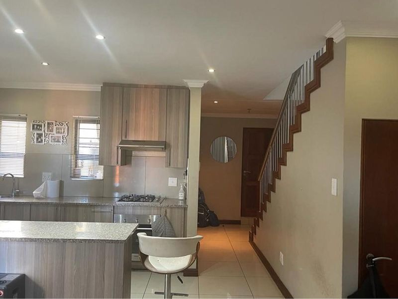 Open plan kitchen featuring wood-look cabinetry, granite countertops, built-in gas hob, and extractor fan, adjacent to a staircase leading to the upper level.