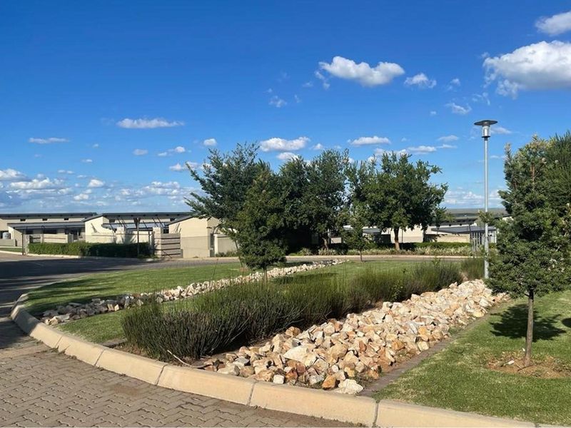 A well-maintained communal garden area within the apartment complex, featuring landscaped lawns, rock garden beds, and paved pathways.