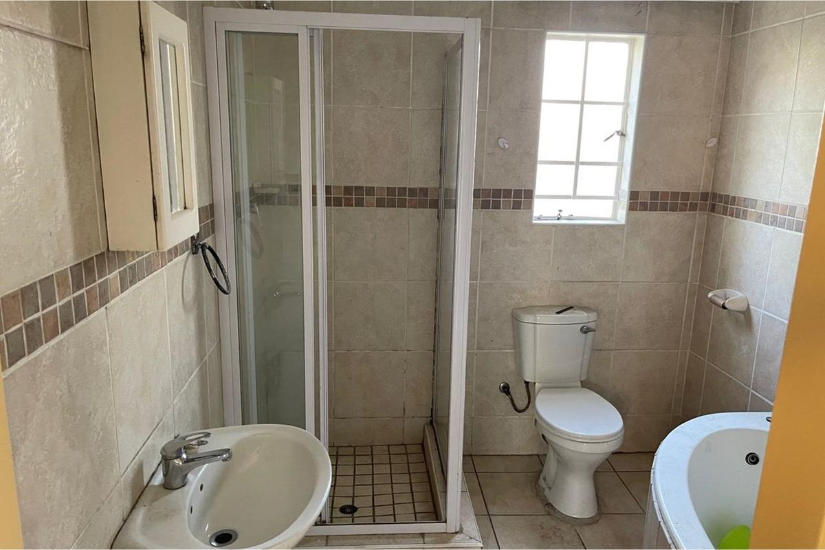 A functional bathroom featuring a corner shower enclosure, a standard toilet, a pedestal basin, and a bathtub with neutral wall tiling.