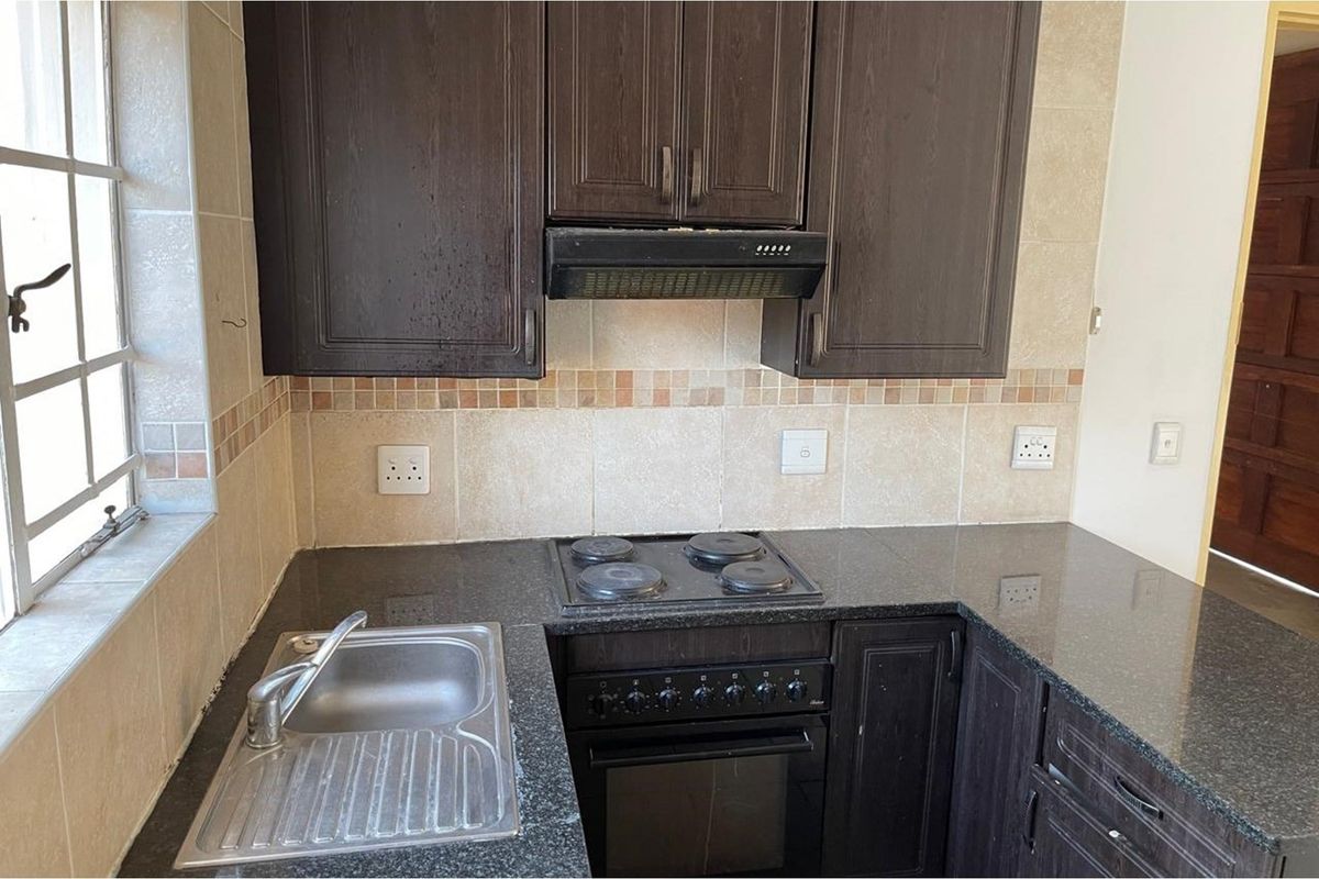 Compact kitchen featuring dark wood cabinetry, granite countertops, a built-in oven with hob, extractor fan, and a stainless steel sink.
