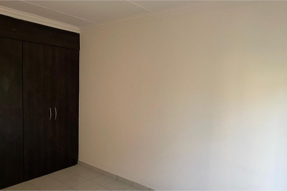 A clean, empty bedroom featuring dark wood built-in cupboards and neutral tiled flooring.
