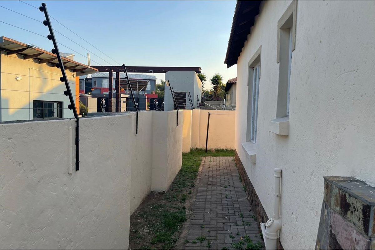 A side exterior walkway featuring paved pathways, perimeter boundary walls with electric fencing, and direct access to the townhouse structure.