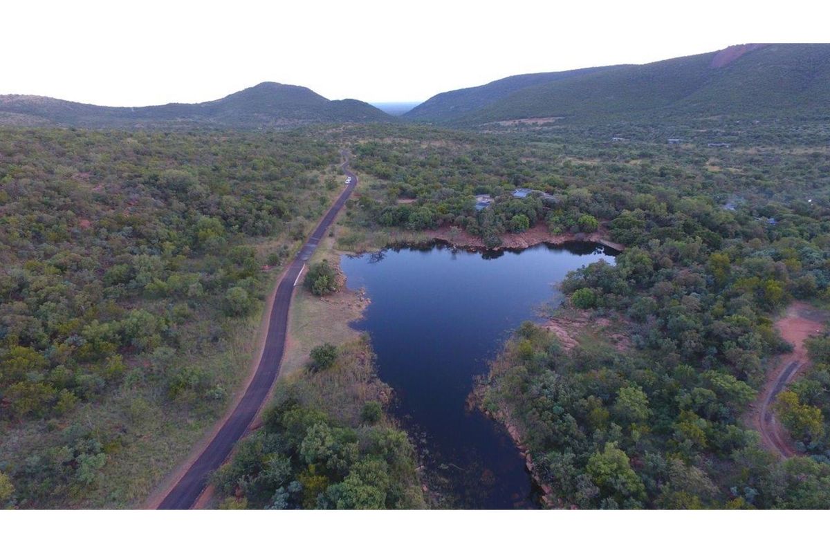 Aerial view of a residential vacant land plot featuring natural landscape, indigenous vegetation, and a scenic dam with surrounding mountain views.