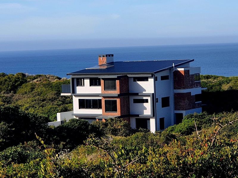 A modern multi-level coastal home featuring a brick and plaster facade, solar panels, and expansive ocean views.