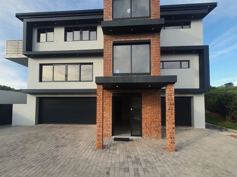 Modern three-story residential property featuring a striking brick and plaster facade, large aluminum windows, and a spacious paved driveway with double garage access.