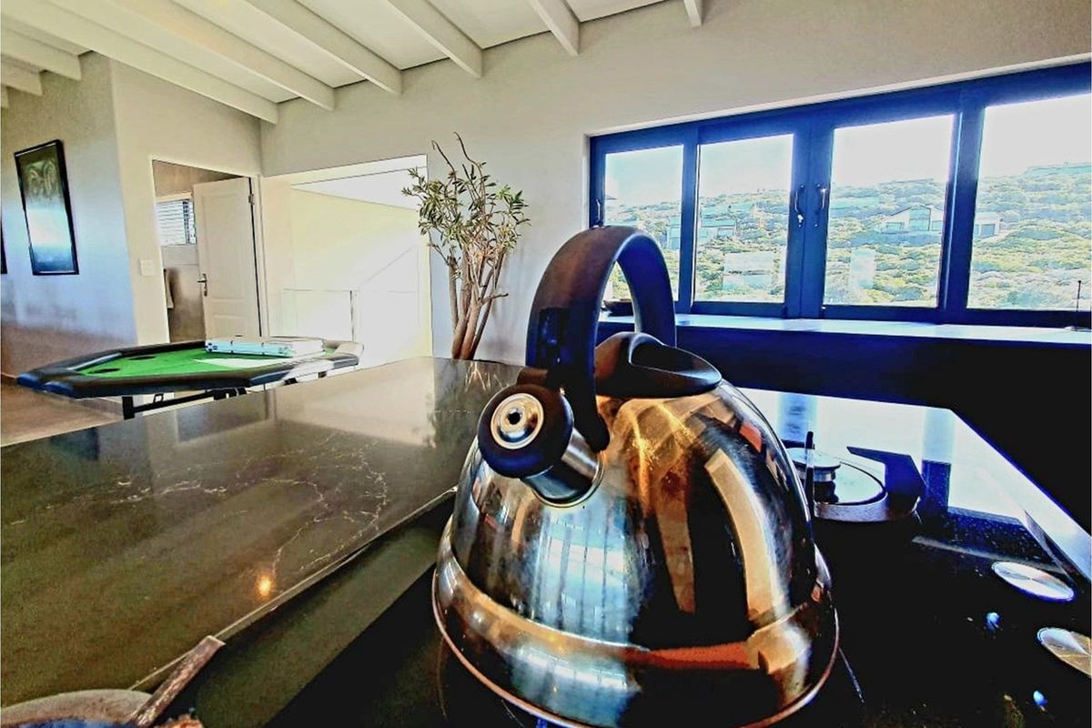 Modern kitchen area featuring a sleek stone countertop, built-in hob, and exposed beam ceiling with views through large aluminium-framed windows.