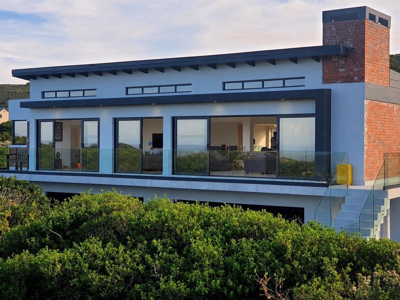 Modern rear elevation featuring expansive sliding glass doors, a glass balustrade balcony, and a distinctive exposed brick chimney.
