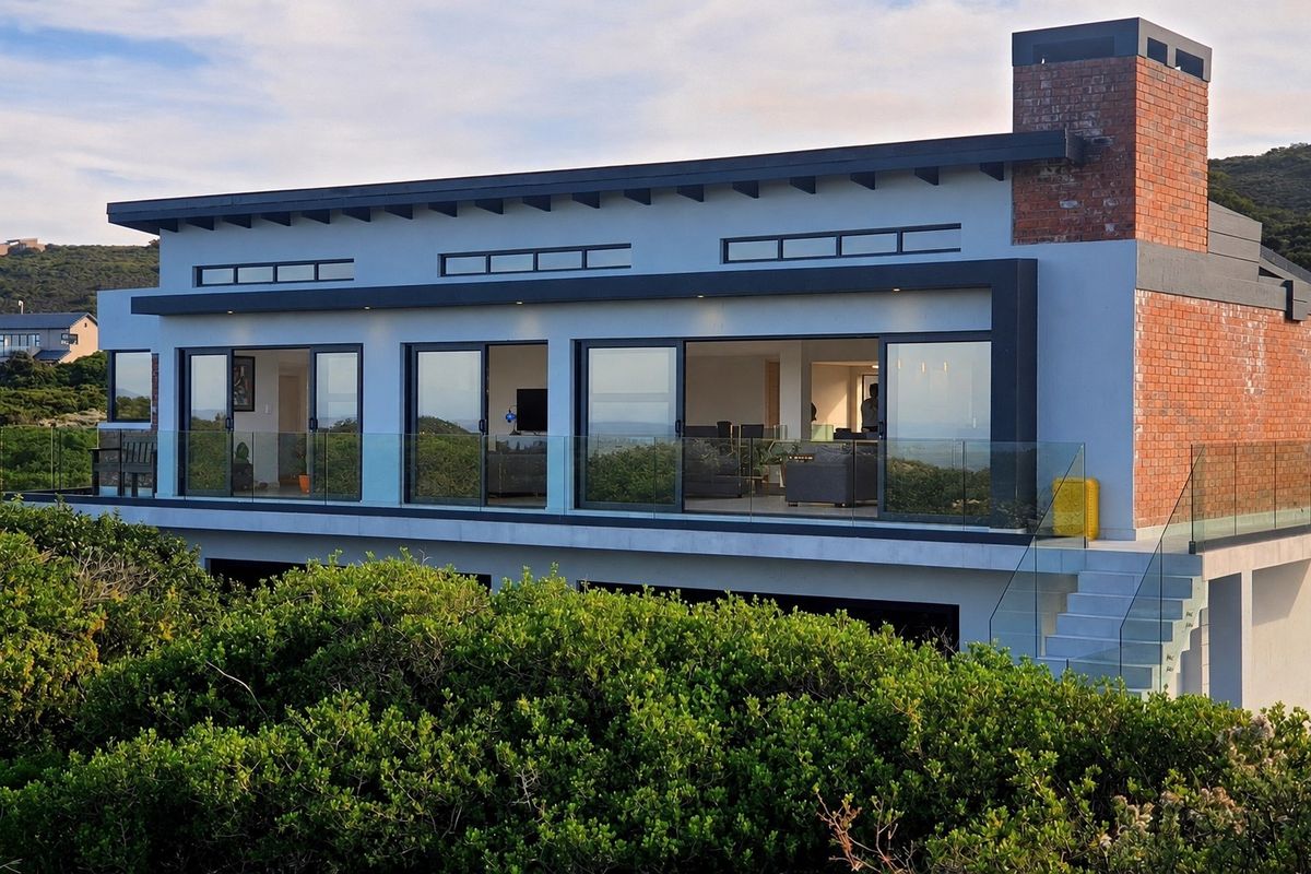 Modern rear elevation featuring expansive sliding glass doors, a glass balustrade balcony, and a distinctive exposed brick chimney.